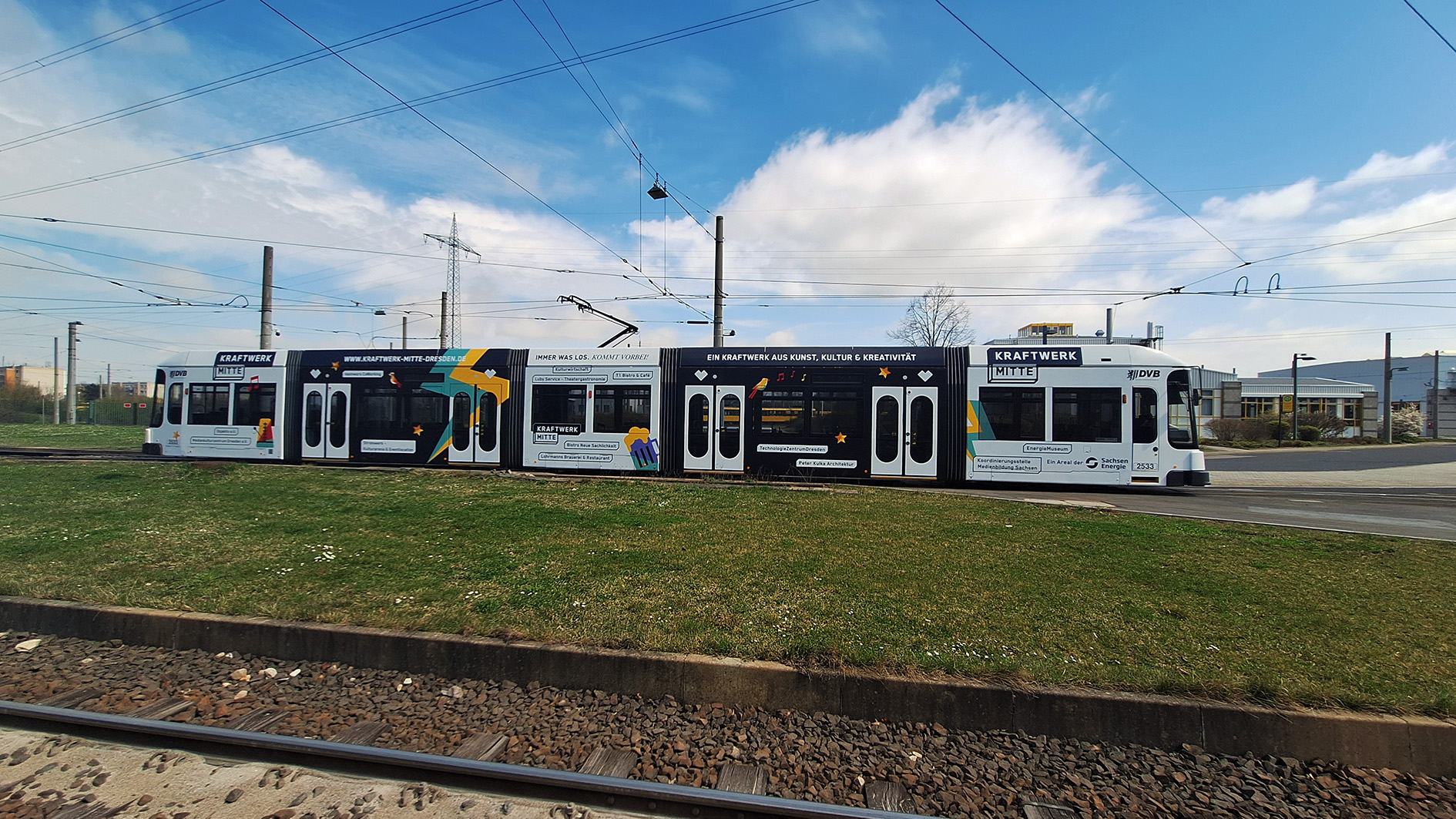 Komplette Seitenansicht einer bunten Straßenbahn mit Kraftwerk-Mitte-Werbung